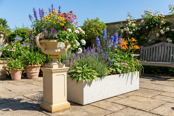 Sunny courtyard garden with a classic stone urn and a rectangular planter overflowing with colourful blooms